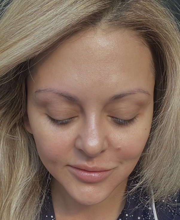 Front view of a woman’s face, eyes looking down, with clear, glowing skin.